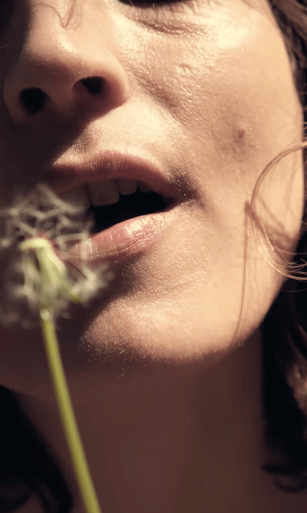 Visage de jeune femme soufflant sur une fleur de pissenlit